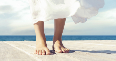 Beautiful and healthy feet of a young girl in white dress on a wooden pier. Vacation, resort and traveling concept.の写真素材