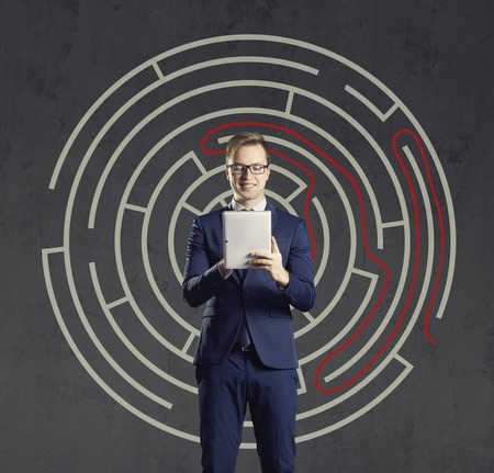 Businessman with computer tablet standing on a labyrinth background. Business, strategy, concept.の写真素材