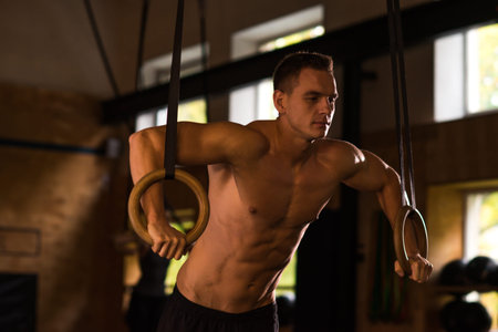 Fit, sporty and athletic sportsman working in a crossfit gym. Man training using gymnastic rings....