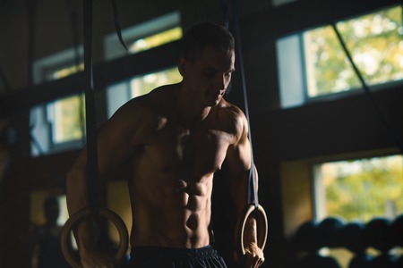Fit, sporty and athletic sportsman working in a crossfit gym. Man training using gymnastic rings. Cross-fit, sports, athletics and fitness concept.の写真素材
