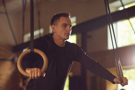 Fit, sporty and athletic sportsman working in a gym. Man training using gymnastic rings. Cross fit,...