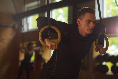 Fit, sporty and athletic sportsman working in a gym. Man training using gymnastic rings. Cross fit, sports, athletics and fitness concept.の写真素材