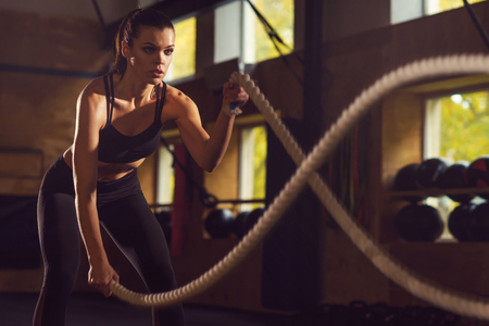 Fit, sporty and athletic sportswoman working in a gym. Woman training using battle ropes. Sports, athletics and fitness concept.の写真素材