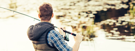 Fisherman with a spinning and bait catching fish on a lake or river. Man on a weekend with a fishing road. Hobby and leisure concept.の写真素材