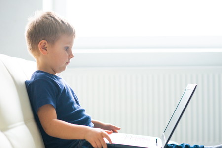 Portrait of happy boy playing with computer. Attractive kid with a laptop at home. Entertainment technology, futuristic gadgets and generation Z concept.の写真素材