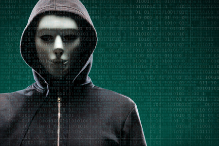 Computer hacker in mask and hoodie over abstract binary background. Obscured dark face. Data thief, internet fraud, darknet and cyber security.の写真素材
