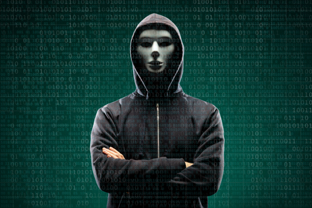 Computer hacker in mask and hoodie over abstract binary background. Obscured dark face. Data thief, internet fraud, darknet and cyber security.の写真素材