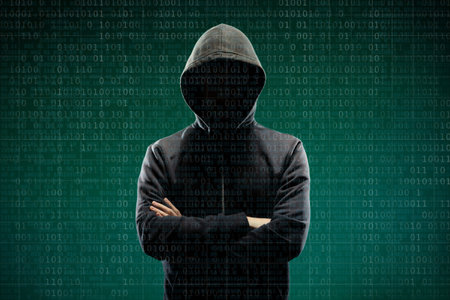 Computer hacker in mask and hoodie over abstract binary background. Obscured dark face. Data thief, internet fraud, darknet and cyber security.の写真素材