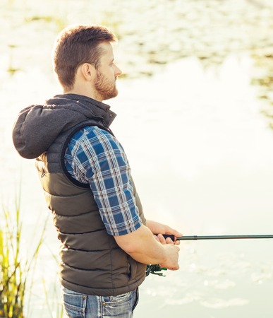 Fisherman with a spinning and bait catching fish on a lake or river. Man on a weekend with a fishing road. Hobby and leisure concept.の写真素材