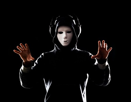 Computer hacker in white mask and hoodie. Obscured dark face. Data thief, internet fraud, darknet and cyber security concept.の写真素材