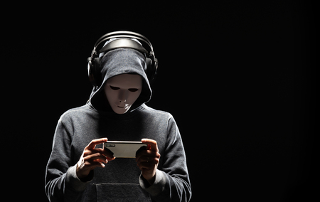 Computer hacker in white mask and hoodie. Obscured dark face. Data thief, internet fraud, darknet and cyber security concept.の写真素材