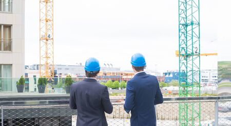 Real estate developers in helmets. New office construction. Confident business men and architect talking in front of modern office building.の写真素材