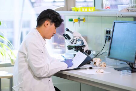 Asian scientist working in lab. Doctor making microbiology research. Laboratory tools: microscope, test tubes, equipment. Biotechnology, chemistry, bacteriology, virology, dna and health care.の写真素材