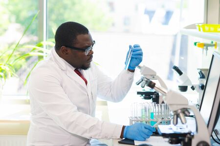 African-american man working in lab. Scientist doctor making medical research. Laboratory tools: microscope, test tubes, equipment. Biotechnology, chemistry, science, experiments and healthcare.の写真素材