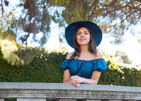 Young and beautiful brunette girl in dress and hat walking outdoor in the park. Nice, France. Summer...