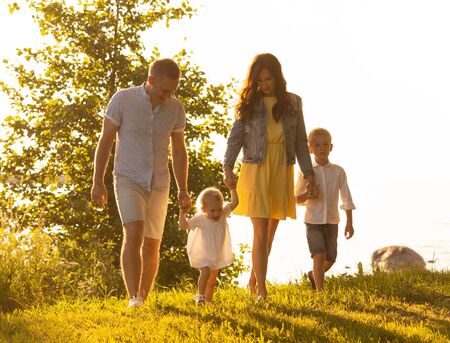 Happy loving family walking outdoor in the light of sunset. Father, mother, son and daughter. Sea and field backgroundの写真素材