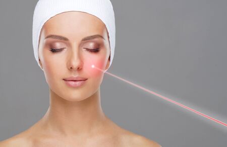 Doctor removing moles using laser ray. Beauty portrait of a young woman. Birthmark removal, plastic surgery, skin lifting and aesthetic medicine.の写真素材