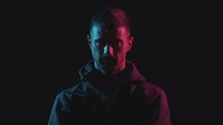 Portrait of computer hacker in hoodie. Obscured dark face in neon light. Data thief, internet fraud,...