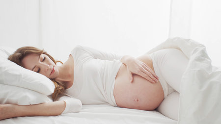 Happy pregnant woman touching her beautiful belly sitting in the bed. Pregnancy, motherhood, and expectation conceptの写真素材