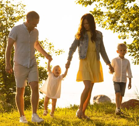 Happy loving family walking outdoor in the light of sunset. Father, mother, son and daughter.の写真素材