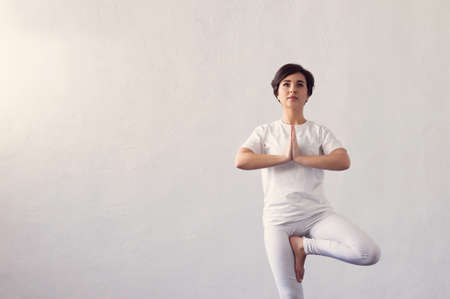 Young and fit woman practicing yoga indoor in the class. Stretching exercise in the day light. Sport, fitness, health care and lifestyle.の写真素材