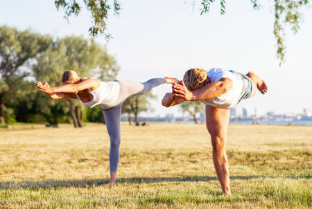 Fit man and beautiful woman practicing yoga outdoor on the grass. Stretching exercise in the sunset....