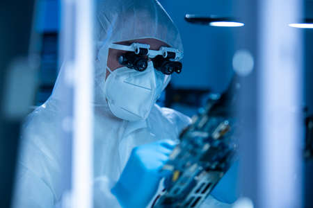 Microelectronics engineer works in a modern scientific laboratory on computing systems and microprocessors. Electronic factory worker is testing the motherboard and coding the firmware.の写真素材