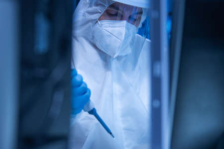 Doctor in protective suit is doing a science experiments and developing vaccine in a modern laboratory. Genetic engineers workplace. The concept of science and medicine.の写真素材