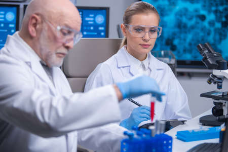 Professor and his young and professional laboratory assistant are doing scientific experiment in a modern laboratory. Genetic engineers workplace. The concept of science, medicine and vaccine.の写真素材