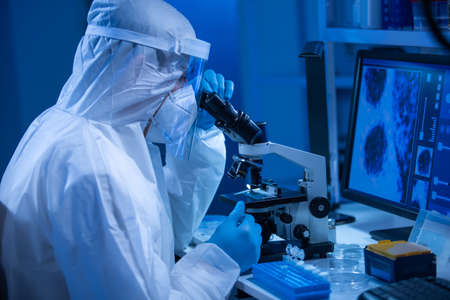 Doctor in protective suit is doing a science experiments and developing vaccine in a modern laboratory. Genetic engineers workplace. The concept of science and medicine.の写真素材
