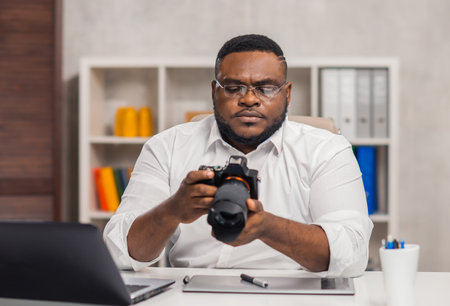 Freelance photographer workplace at home office. Young African-American man works using a computer, graphics tablet and other devices. Remote job.の写真素材