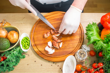 Young chef is cutting octopus in a modern kitchen. The man prepares food at home. Cooking healthy...