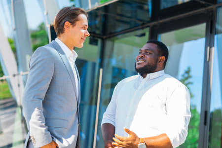 African-American businessman and his colleague in front of modern office building. Financial investors are talking outdoor. Banking and business concept.の写真素材