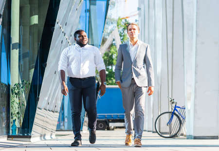 African-American businessman and his colleague in front of modern office building. Financial investors are talking outdoor. Banking and business concept.の写真素材