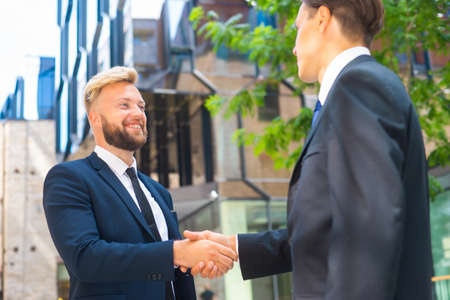 Confident businessman and his colleague are shaking hands in front of modern office building. Financial investors outdoor. Banking and business.の写真素材