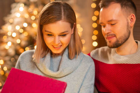 Young loving couple celebrating Christmas at home. Young man and his attractive girlfriend in a home interior with a Christmas tree.の写真素材