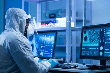 African-american doctor in protective suit is doing a science experiments and developing vaccine in a modern lab. Laboratory assistant workplace. The concept of science and medicine.の写真素材