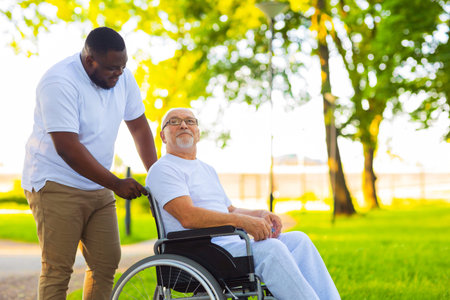 Caregiver and old man in a wheelchair. Professional nurse and patient walking outdoor in the park at...