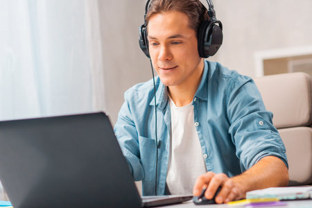 Young man in headphones works on a laptop computer at home. Remote work and education concept.