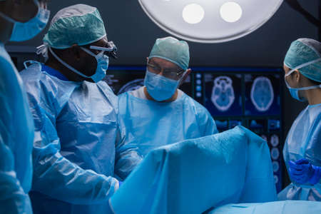 Multiracial team of professional medical surgeons performs the surgical operation in a modern hospital. Doctors are working to save the patient. Medicine, health and neurosurgery.の写真素材
