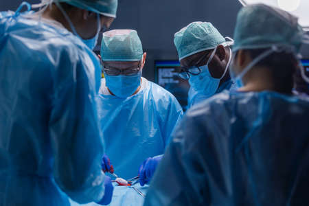 Multiracial team of professional medical surgeons performs the surgical operation in a modern hospital. Doctors are working to save the patient. Medicine, health, cardiology and transplantation.の写真素材
