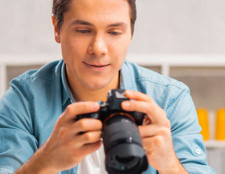 Freelance photographers workplace. A young man with a camera is sitting at a table and watching photos. Remote work concept.の写真素材