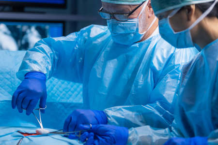 Multiracial team of professional medical surgeons performs the surgical operation in a modern hospital. Doctors are working to save the patient. Medicine, health, cardiology and transplantation.の写真素材