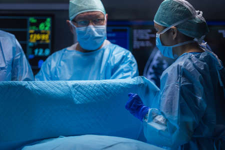 Multiracial team of professional medical surgeons performs the surgical operation in a modern hospital. Doctors are working to save the patient. Medicine, health and neurosurgery.の写真素材