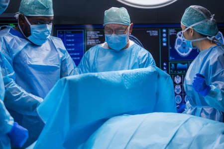 Multiracial team of professional medical surgeons performs the surgical operation in a modern hospital. Doctors are working to save the patient. Medicine, health and neurosurgery.の写真素材