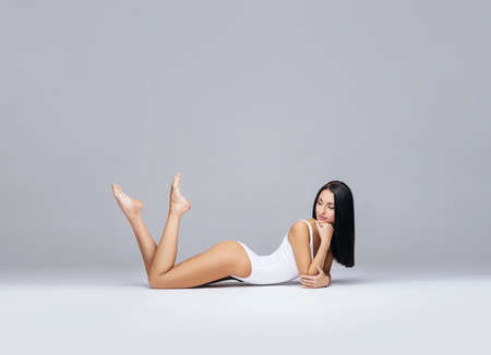 Attractive and slender brunette girl in white underwear posing in studio. Healthy lifestyle, sport and body care concept.の写真素材