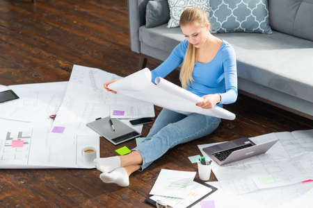 Young woman works with documents using a laptop while sitting on the floor at home. Student, entrepreneur or freelancer girl working or studying remotely via internet.の写真素材