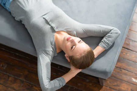 Young beautiful girl lies on a sofa. Happy blond woman is resting at home.