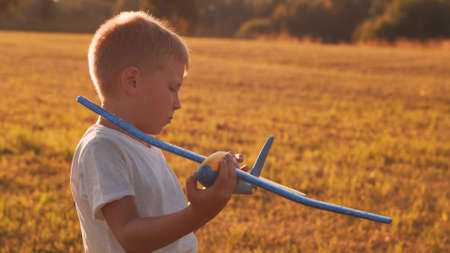 Boy plays with a toy plane in a field at sunset. The concept of childhood, freedom and inspiration.の写真素材