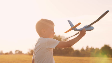 Boy plays with a toy plane in a field at sunset. The concept of childhood, freedom and inspiration.